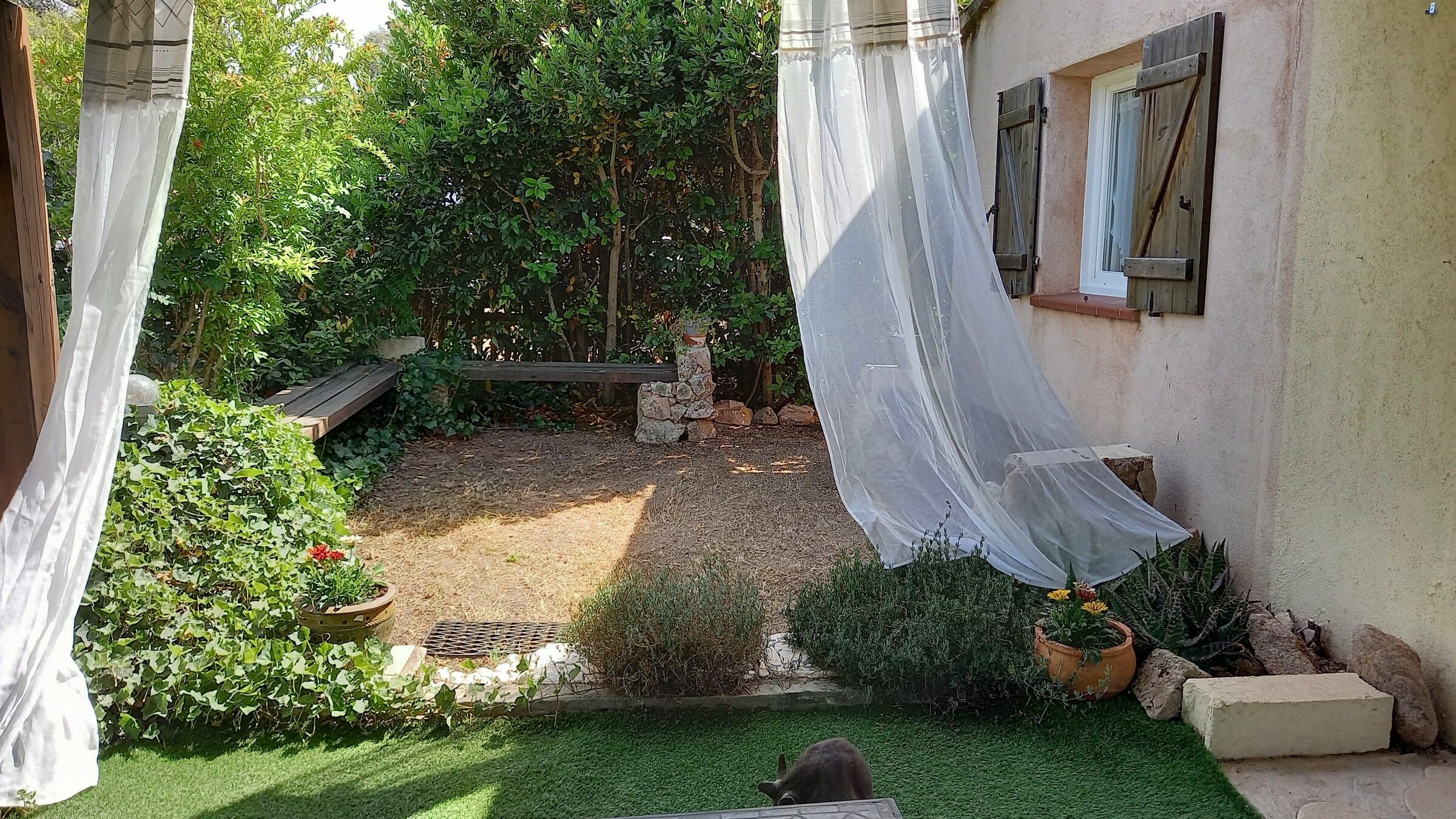 Le jardin et la façade aux volets de bois, vus depuis la terrasse