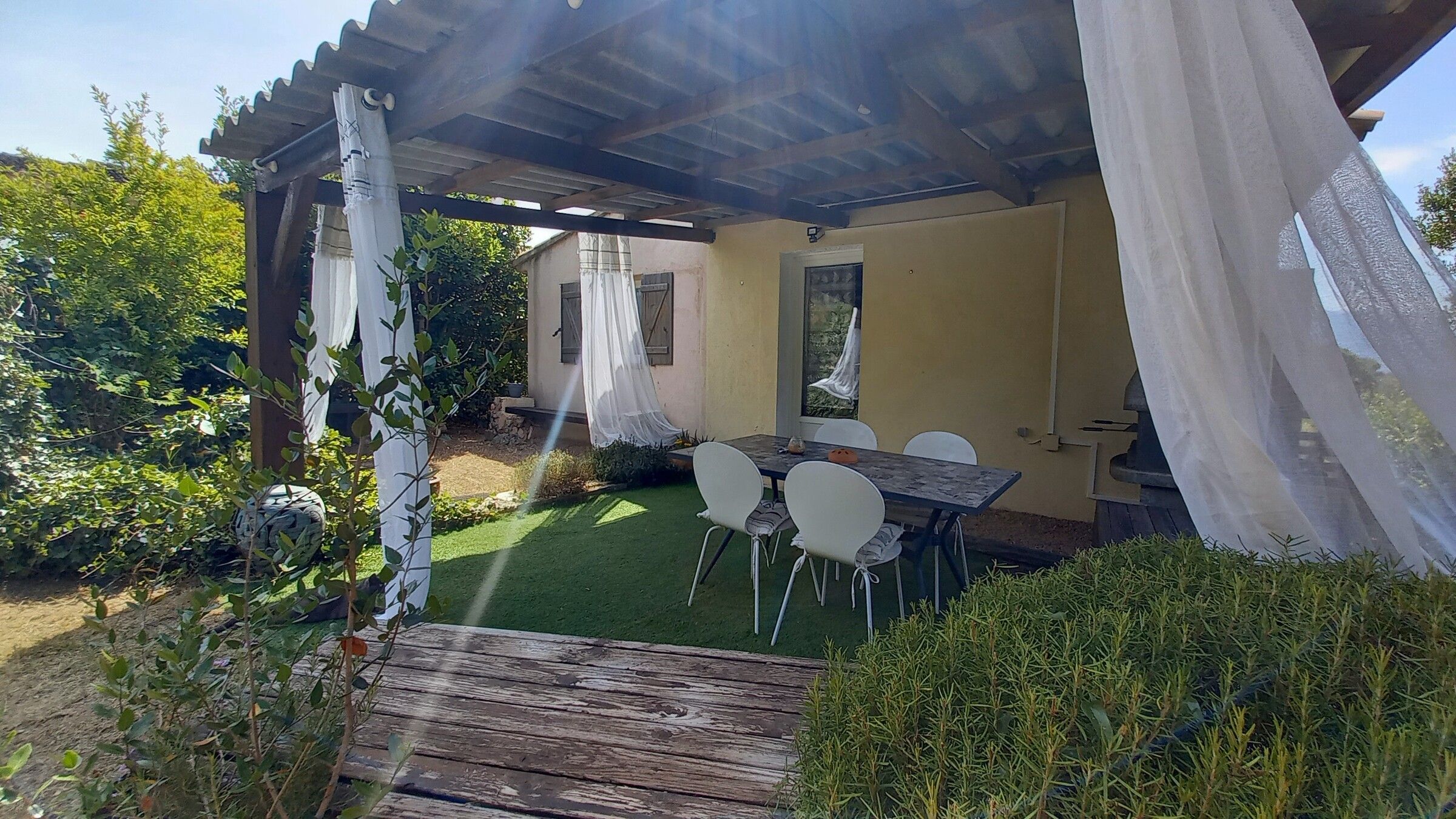 La terrasse couverte à contre-jour, les voilages traversés par le soleil de fin d'après-midi